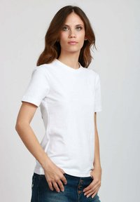 T-shirt bianco in cotone con maniche corte, colletto rotondo e design aderente. Il tessuto appare liscio con cuciture minime e nessun motivo visibile.