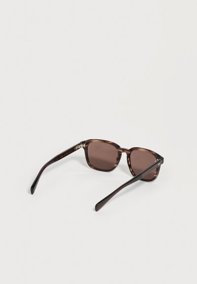 Lunettes de soleil rectangulaires en écaille de tortue marron avec verres foncés reposant ouvertes sur un fond blanc.