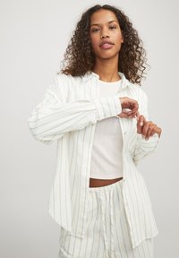Camisa abotonada de manga larga ligera en blanco con rayas doradas verticales; presenta un ajuste relajado y una textura de tela; diseño con cuello.