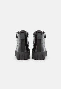 Črne lakirane gležnjače z bočnimi zadrgami, teksturiranimi elastičnimi paneli in gumijastimi podplati z rebrastimi vzorci.