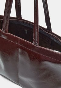 Braune Leder-Totetasche mit zwei Griffen, einem Reißverschluss oben und einer sichtbaren Reißverschlusstasche im Inneren.