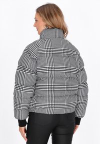 Giacca imbottita con un motivo houndstooth bianco e nero, dotata di un colletto alto, polsini elastici e un design cropped.