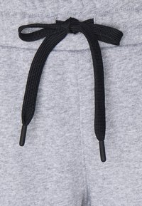 Grå sweatpants i en texturerad tyg, med en svart snörning knuten i midjan och plastspetsar i ändarna.