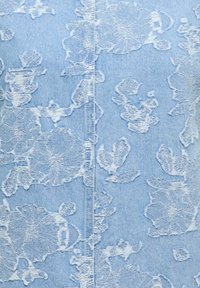 Denim bleu clair avec des motifs floraux brodés blancs et une couture de couture centrale visible descendant le tissu.