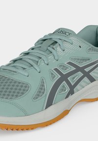 Ανοιχτό πράσινο παπούτσι τρεξίματος Asics με γκρι λογότυπο, διχτυωτά πάνελ, κορδόνια και πορτοκαλί λαστιχένια σόλα, τοποθετημένο σε γωνία για να δείχνει πλαϊνές και μπροστινές λεπτομέρειες.