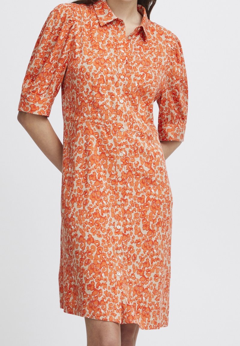 Robe orange à manches courtes avec un devant à boutons, ornée d'un motif floral dans des teintes variées d'orange sur un fond clair.