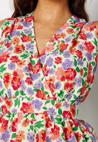 Vestido floral con un diseño de escote en V, que presenta una base blanca adornada con vibrantes flores rojas, púrpuras y verdes. Textura arrugada, cintura ajustada.