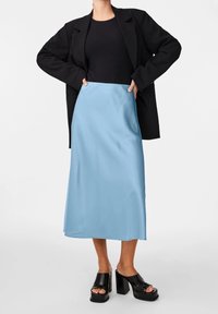 Vaaleansininen satiininen pitkä hame, yhdistetty mustaan istuvaan toppiin ja ylisuurikokoiseen bleiseriin; asussa paksupohjaiset mustat sandaalit.