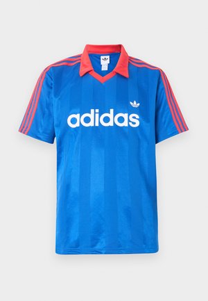 Sinine Adidas lühikeste varrukatega spordisärk punase krae ja triipudega õlgadel, millel on valge Adidas logo ja kolmeleheline embleem rinnal.