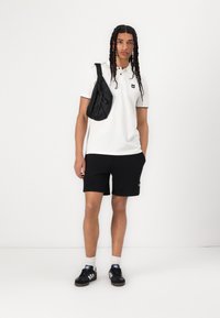Hvit polo-skjorte med en liten logo, svarte shorts og en svart crossover-veske. Svarte sneakers med tre hvite striper, hvite sokker.