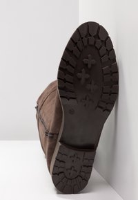 Bottine en daim marron avec une semelle en caoutchouc texturée présentant un motif de bande de roulement. Détail zippé sur le côté et taille indiquée en 37.