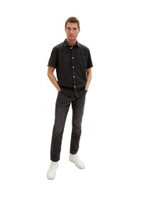 Camicia nera a maniche corte con bottoni, taschino, abbinata a jeans scuri e sneaker bianche. Design semplice e casual, texture del tessuto morbida.
