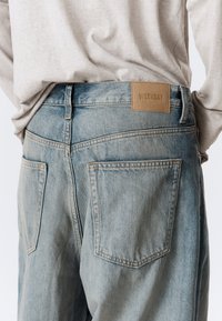 Ξεθωριασμένο μπλε τζιν με δερμάτινη ετικέτα "WEEKDAY" στο πίσω μέρος. Η σχεδίαση περιλαμβάνει δύο πίσω τσέπες και ορατές ραφές.