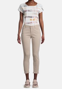 Jean beige court avec ourlets effilochés, associé à un haut à manches courtes avec une base blanche et des rayures horizontales multicolores.