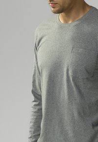 Szara, długą rękaw T-shirt wykonany z miękkiego materiału, z okrągłym dekoltem i kieszonką na lewej piersi, prezentujący delikatną teksturę.