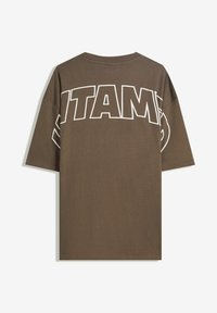 Barna, nagy méretű pamut póló, fehér, vastag betűkkel a hátán "ITAM" felirattal és kerek nyakkivágással. Rövid ujjú.