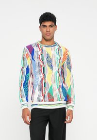 Πλεκτό πουλόβερ με πολύχρωμο γεωμετρικό μοτίβο σε μπλε, κόκκινο, πράσινο και κίτρινο. Ριμπάριστο μανίκι και στρίφωμα, στρογγυλή λαιμόκοψη, υφή υφάσματος.