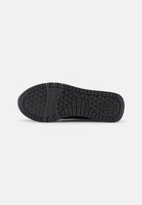 Black sneaker sole with textured rubber grips, featuring a hexagonal pattern and a logo. Shape is flat with defined grooves for traction.