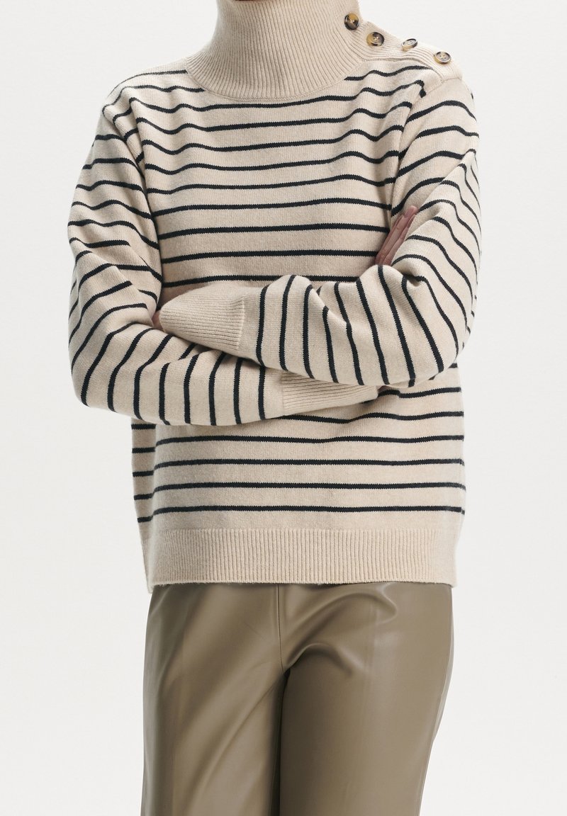 Suéter de rayas beige con líneas marinas, cuello alto y dobladillo acanalado; presenta detalles de botones en el hombro y una suave textura de punto.