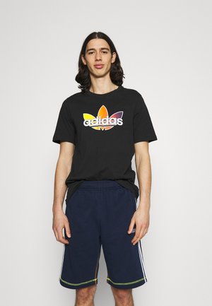 T-shirt nera in cotone con logo Adidas multicolore e design a foglia, abbinata a pantaloni corti blu navy con strisce bianche e accenti verdi.
