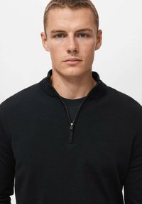 Schwarzer Halbzip-Pullover aus strukturiertem Material, mit Stehkragen und einem kleinen silbernen Reißverschluss. Einfaches Design, taillierte Silhouette.