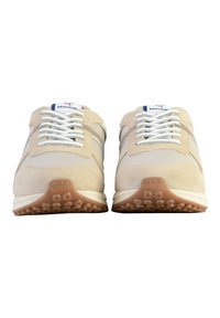 Baskets de sport beiges avec une tige en daim et en tissu, lacets blancs, semelle en caoutchouc marron foncé et détail de logo sur la languette.