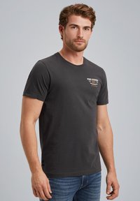 Black cotton t-shirt with a crew neckline, short sleeves, and a small printed logo on the left chest. Worn with blue denim jeans.