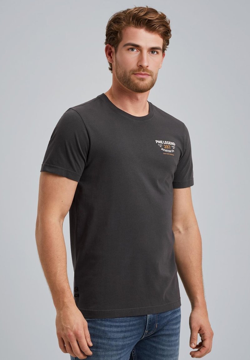 Sort bomuld t-shirt med rund hals, korte ærmer og et lille trykt logo på venstre bryst. Bæres med blå denimjeans.