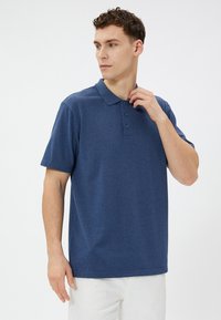 Marineblå polo-shirt med blød tekstur, korte ærmer, tre-knaps placket og klassisk krave. Båret med hvide bukser.
