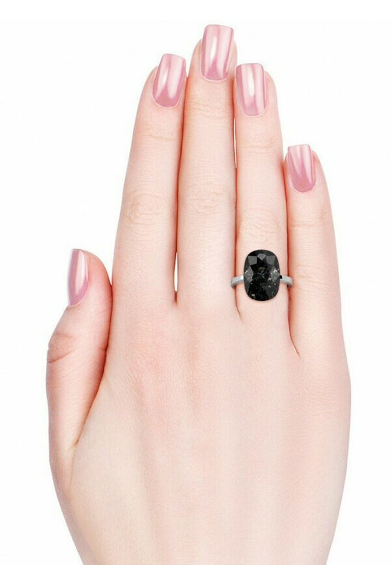 Schwarzer ovaler Edelsteinring auf einem silbernen Band, präsentiert an einer Hand mit einem hellrosanen Nageldesign. Glatte Textur und facettierte Oberfläche des Steins.