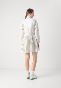 Lättvit klänning med veckad kjol, hög krage och elastisk midja. Slät textur och minimalistisk design. Buren med vita sneakers.