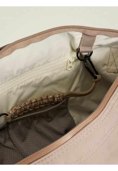Beige taske indvendig med et stoffor, en lynlåslomme, et mesh rum og en lysebrun fletdetalje. Indeholder to tilslutningspunkter.