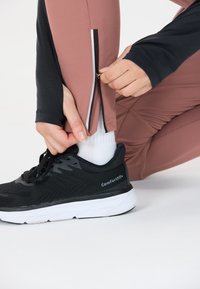 Zwarte sportshoe met een witte zool. Close-up van een persoon die een roze legging met een zwart shirt met lange mouwen ritst; textuur zichtbaar.