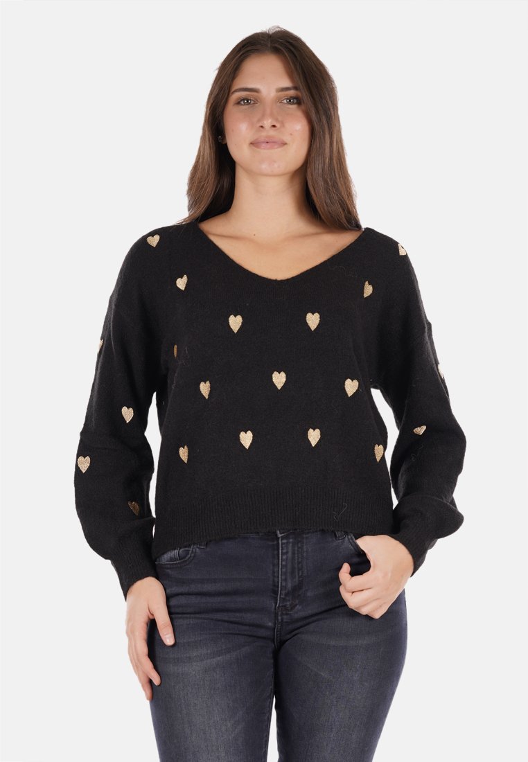 Maglione nero con scollo a V, con motivi a cuore dorati, polsini e orlo a coste. Il tessuto appare morbido eTexture. Indossato con jeans scuri.