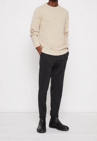Beżowy sweter wykonany na drutach z okrągłym dekoltem, zestawiony z ciemnymi spodniami slim fit i czarnymi botkami za kostkę, charakteryzującymi się gładką teksturą i subtelnymi detalami.