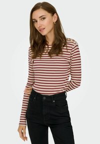 Rood en crèmekleurig gestreept longsleeve top, geribbelde textuur, ronde halslijn, met gouden knoopaccenten op de schouder. Draagt met zwarte high-waisted jeans.