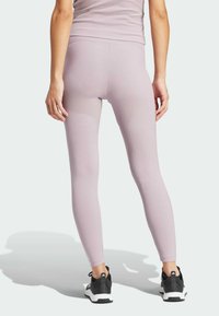 Person klädd i ljuslila ribbade leggings och matchande topp, stående med händerna avslappnat vid sidorna, svarta och vita sportskor synliga.