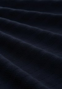 Granatowa, teksturowana tkanina z diagonalnymi prążkami, ukazująca miękki splot i subtelny blask na gładkich, złożonych warstwach.