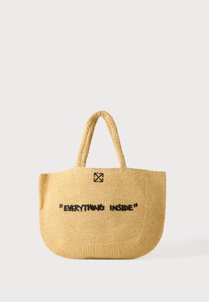 Un bolso tote tejido color marrón claro con dos asas, un pequeño emblema negro con flechas cruzadas y las palabras «Everything Inside» en el frente.