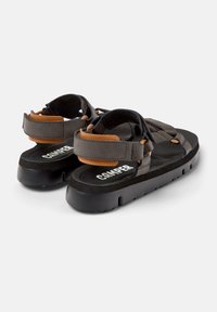 Sandalias negras con correas grises y acentos marrones, que cuentan con cierres ajustables de Velcro, una plantilla texturizada y una suela gruesa negra.