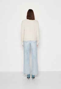 Pull beige côtelé à manches longues, associé à un jean large bleu clair et des escarpins pointus bleu sarcelle, vu de dos.