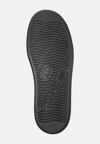 Suela de zapato de goma negra con un patrón de olas texturizado, que presenta un logo circular y la marca "CAMPER" en relieve. Acabado suave, bordes ligeramente curvados.