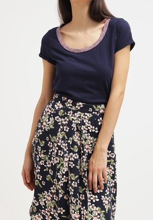 Mujer con una blusa de manga corta azul marino con borde rosa en el escote y una falda de talle alto azul marino con estampado floral blanco y rosa.