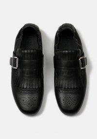 Zwarte leren schoenen met een franjeontwerp en een gesp-sluiting. Beschikt over geperforeerde details op de neus en een elastische enkel voor comfort.