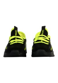 Zapatos deportivos negros con cordones y acentos amarillos brillantes. Presentan un upper de tela texturizada y una suela de goma. Branding en el talón.