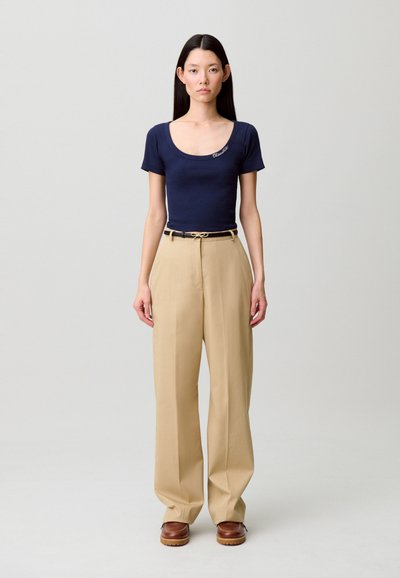 Top de manga corta azul marino con escote redondo y detalle sutil de logo, combinado con pantalones beige de talle alto con corte amplio y cinturón.