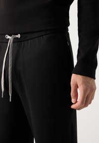 Sorte joggebukser med elastisk talje og sølvfarvet snor. Side lomme synlig, med et lille mærkelabel på sømmen.