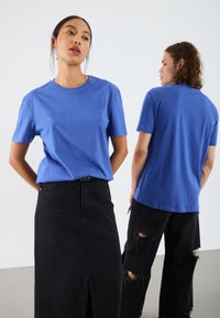 Tricou din bumbac albastru cu mâneci scurte, asortat cu fustă din denim negru și blugi negri deteriorați. Ambele ținute au o croială lejeră.