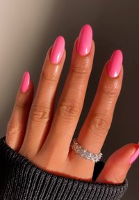 Klarröda ovalformade naglar med en glänsande finish, prydda med en silvring med klara ädelstenar, mot en mörk texturerad tygbakgrund.