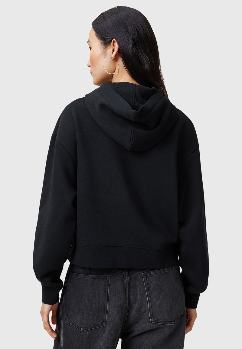 Schwarze, kurze Kapuzenjacke aus weichem Stoff. Eigenschaften sind große Ballonärmel und gerippte Bündchen. Getragen mit dunklen Jeans.
